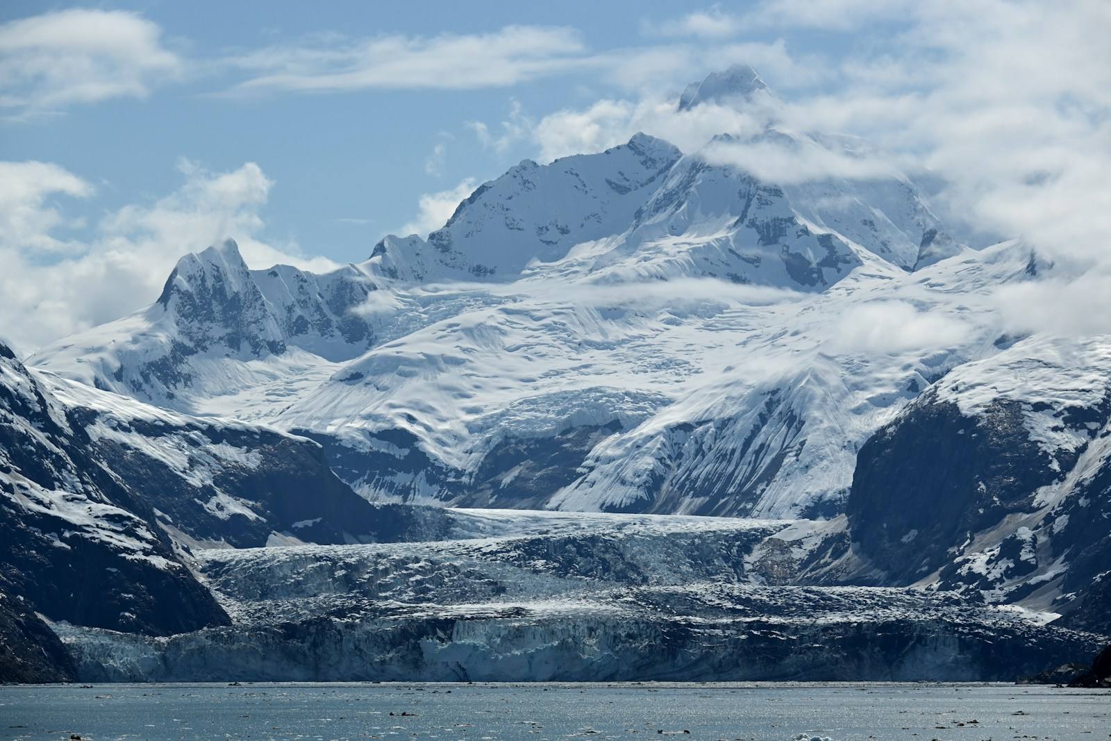 A dramatic view of towering snow-covered mountains and the massive tidewater glacier flowing into the bay in Glacier Bay National Park, Alas