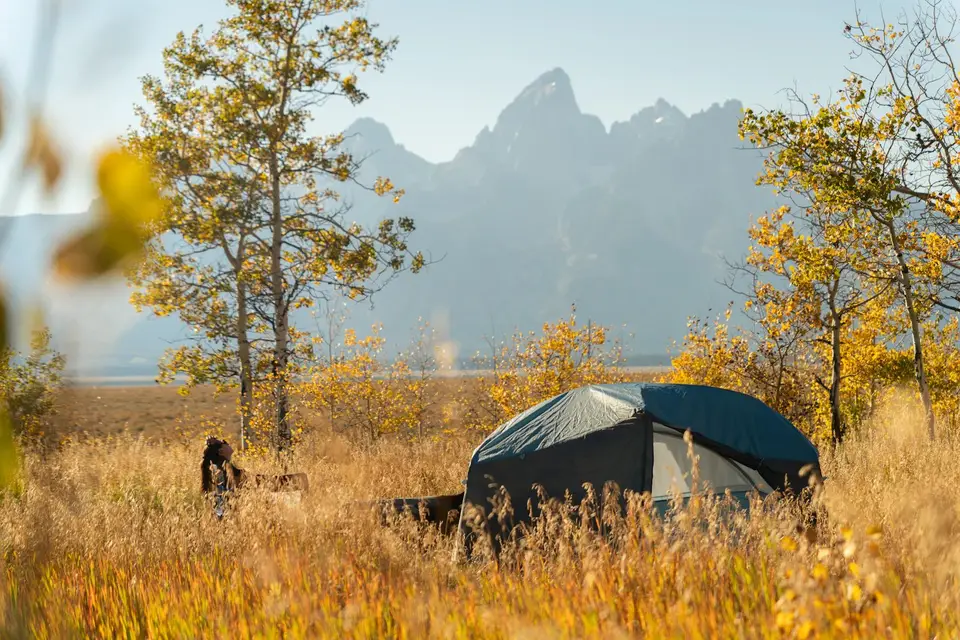 A dome tent among golden aspens and grass with the Teton Range behind