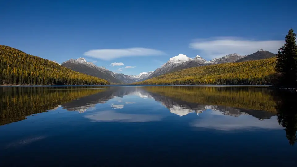 Calm Bowman Lake reflecting forested ridges and snowy peaks