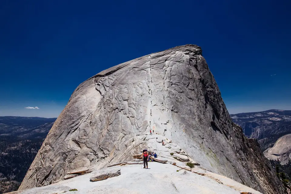 A hiker standing on the bare granite summit of Half Dome