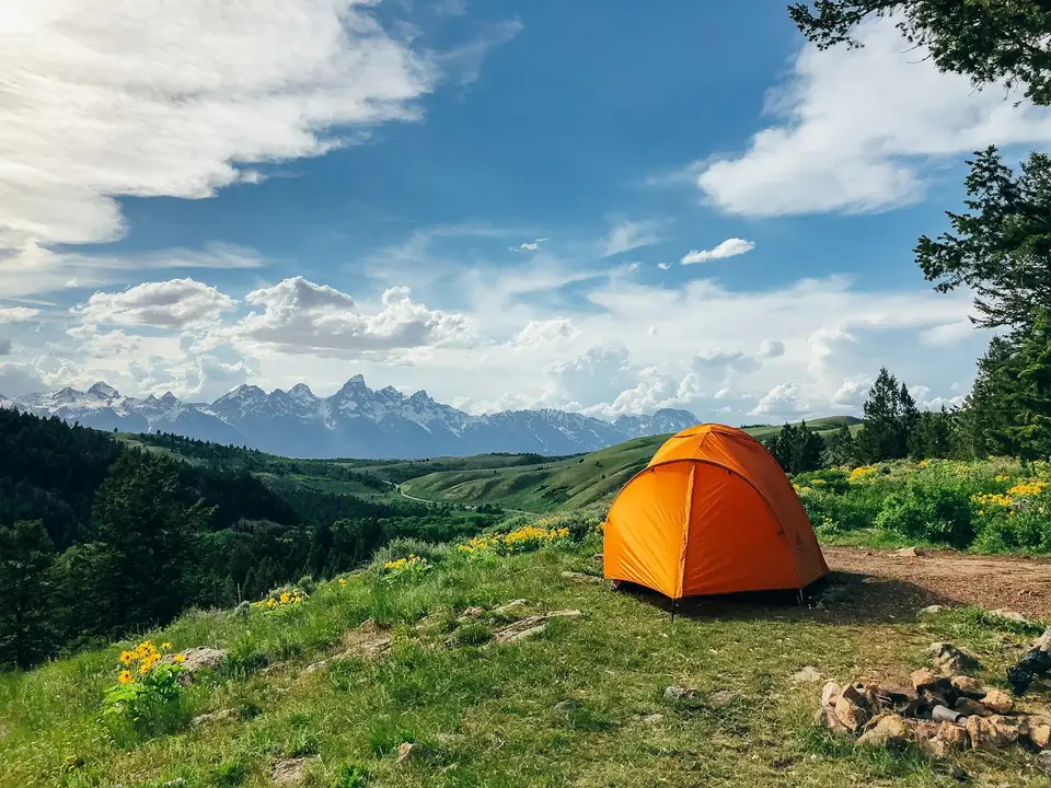 An orange tent on a grassy hillside with the Teton Range in the distance