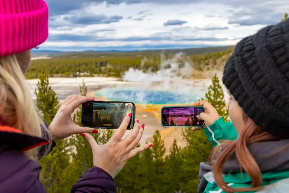 Two visitors photograph Grand Prismatic Spring with their phones from the overlook