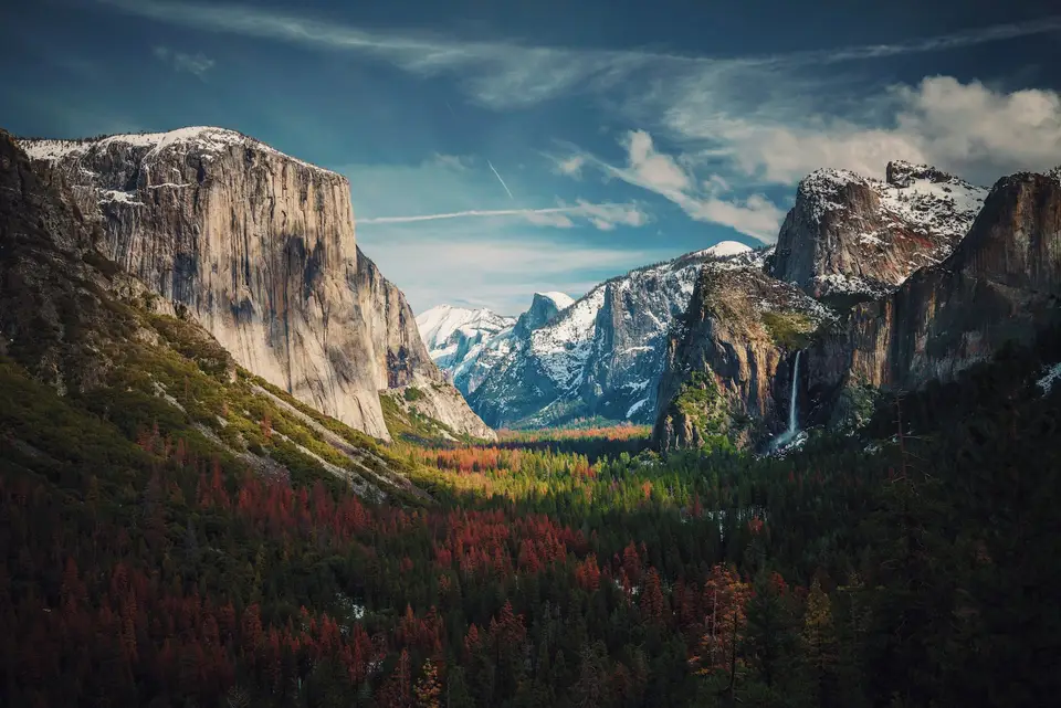 Snow-dusted granite cliffs and a waterfall above forest